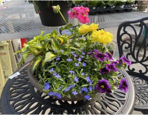 Planter filled with different flowers sitting on top of a outside patio tabke