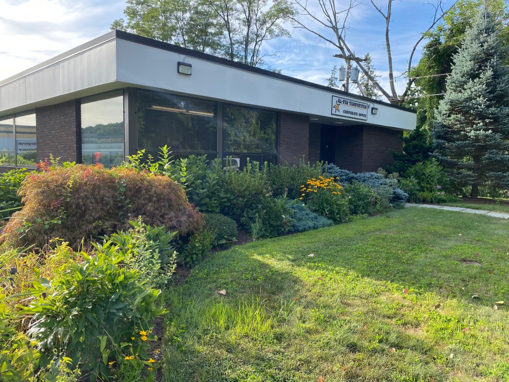 1CFD64BE-F50D-478A-804A-676E143B02B1 | Larson’s Garden Center and Landscaping Exterior view of a corporate office building surrounded by colorful shrubs and greenery.